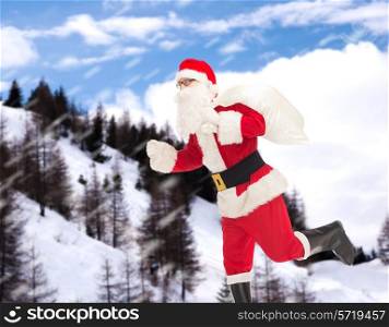 christmas, holidays and people concept - man in costume of santa claus running with bag over snowy mountains background