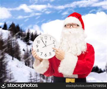 christmas, holidays and people concept - man in costume of santa claus with clock showing twelve pointing finger over snowy mountains background
