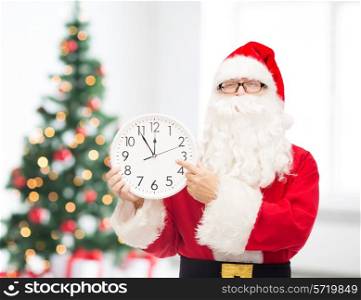 christmas, holidays and people concept - man in costume of santa claus with clock showing twelve pointing finger over living room with tree background