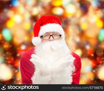 christmas, holidays and people concept - man in costume of santa claus blowing on palms over red lights background