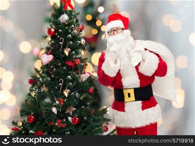 christmas, holidays and people concept - man in costume of santa claus with bag and christmas tree making hush gesture over lights background