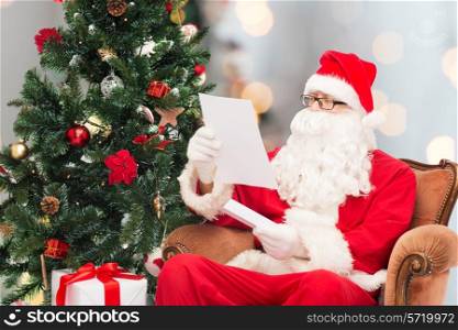christmas, holidays and people concept - man in costume of santa claus with letter and christmas tree sitting in armchair over lights background