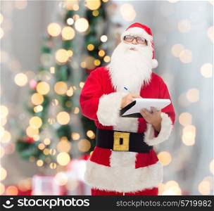 christmas, holidays and people concept - man in costume of santa claus with notepad and pen over tree lights background