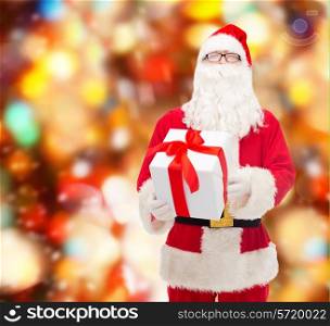 christmas, holidays and people concept - man in costume of santa claus with gift box over red lights background