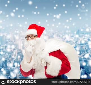 christmas, holidays and people concept - man in costume of santa claus with bag making hush gesture over snowy city background