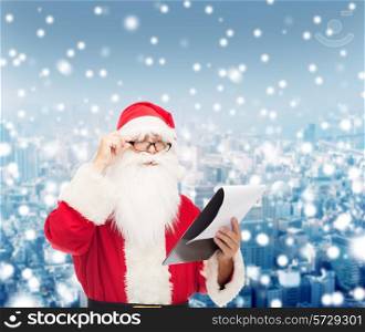 christmas, holidays and people concept - man in costume of santa claus with notepad over snowy city background