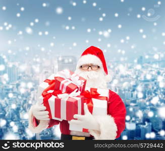 christmas, holidays and people concept - man in costume of santa claus with gift boxes over snowy city background