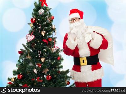 christmas, holidays and people concept - man in costume of santa claus with bag and christmas tree making hush gesture over blue lights background