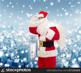 christmas, holidays and people concept - man in costume of santa claus with bag looking far away over snowy city background