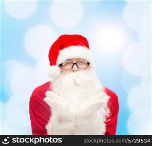 christmas, holidays and people concept - man in costume of santa claus blowing on palms over blue lights background