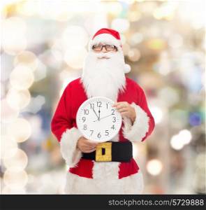 christmas, holidays and people concept - man in costume of santa claus with clock showing twelve pointing finger over lights background