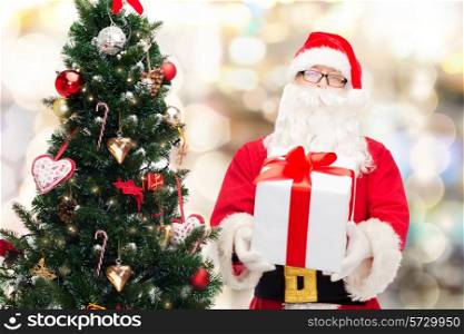 christmas, holidays and people concept - man in costume of santa claus with gift box and tree over lights background