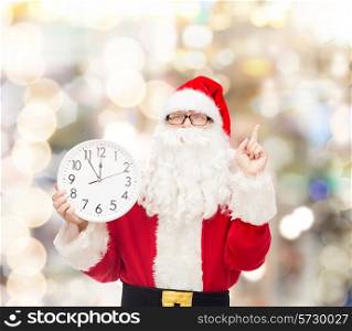 christmas, holidays and people concept - man in costume of santa claus with clock showing twelve pointing finger up over lights background