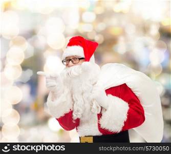 christmas, holidays and people concept - man in costume of santa claus with bag pointing finger over lights background