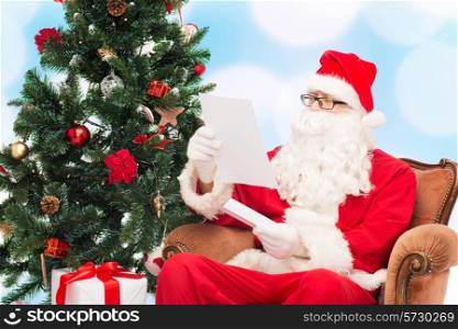 christmas, holidays and people concept - man in costume of santa claus with letter and christmas tree sitting in armchair over blue lights background