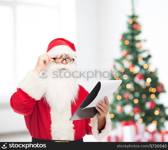 christmas, holidays and people concept - man in costume of santa claus with notepad over living room and tree background