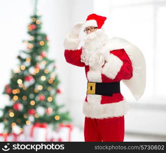 christmas, holidays and people concept - man in costume of santa claus with bag looking far away over living room and tree background