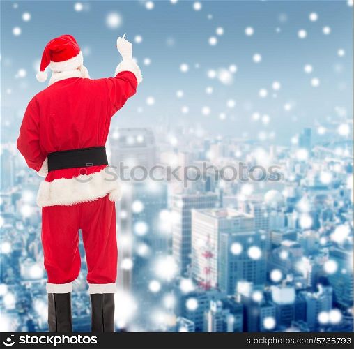 christmas, holidays and people concept - man in costume of santa claus writing something from back over snowy city background