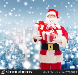 christmas, holidays and people concept - man in costume of santa claus with gift boxes over snowy city background