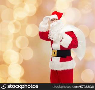 christmas, holidays and people concept - man in costume of santa claus with bag looking far away over beige lights background