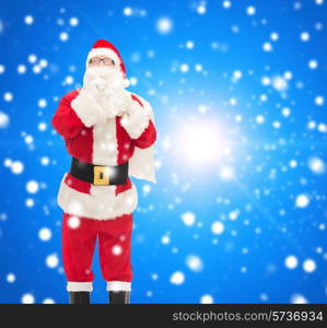 christmas, holidays and people concept - man in costume of santa claus with bag making hush gesture over blue snowy background
