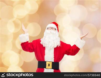 christmas, holidays and people concept - man in costume of santa claus with raised hands over beige lights background