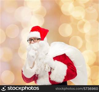 christmas, holidays and people concept - man in costume of santa claus with bag making hush gesture over beige lights background
