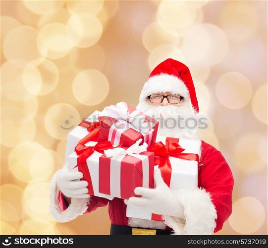 christmas, holidays and people concept - man in costume of santa claus with gift boxes over beige lights background