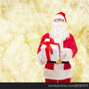 christmas, holidays and people concept - man in costume of santa claus with gift box over yellow lights background
