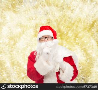 christmas, holidays and people concept - man in costume of santa claus with bag making hush gesture over yellow lights background