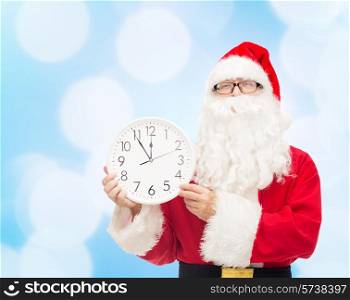 christmas, holidays and people concept - man in costume of santa claus with clock showing twelve over blue lights background