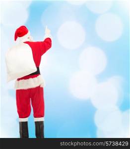 christmas, holidays and people concept - man in costume of santa claus with bag pointing finger from back over yellow lights background over blue lights background