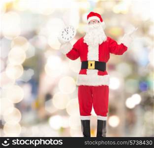 christmas, holidays and people concept - man in costume of santa claus with clock showing twelve over lights background