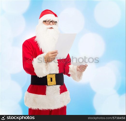 christmas, holidays and people concept - man in costume of santa claus reading letter over blue lights background