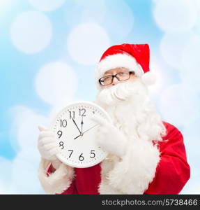 christmas, holidays and people concept - man in costume of santa claus with clock showing twelve over blue lights background