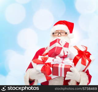 christmas, holidays and people concept - man in costume of santa claus with gift boxes over blue lights background