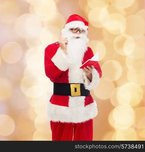 christmas, holidays and people concept - man in costume of santa claus with notepad and pen over beige lights background