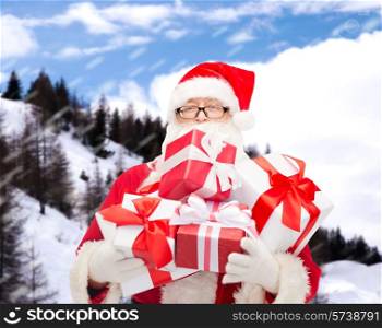 christmas, holidays and people concept - man in costume of santa claus with gift boxes over snowy mountains background
