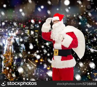 christmas, holidays and people concept - man in costume of santa claus with bag looking far away over snowy night city background