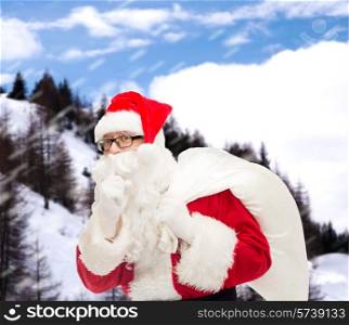 christmas, holidays and people concept - man in costume of santa claus with bag making hush gesture over snowy mountains background