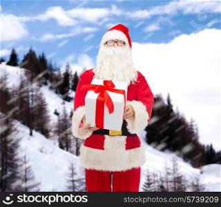 christmas, holidays and people concept - man in costume of santa claus with gift box over snowy mountains background