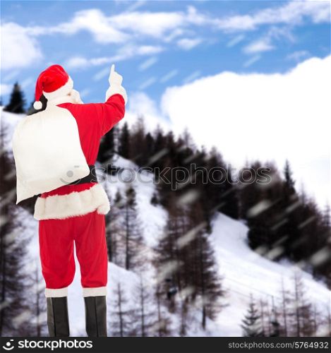christmas, holidays and people concept - man in costume of santa claus with bag pointing finger from back over snowy mountains background