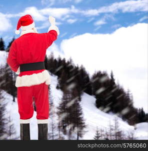 christmas, holidays and people concept - man in costume of santa claus writing something from back over snowy mountains background