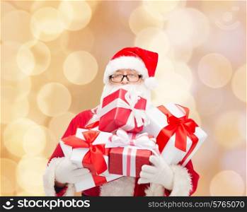 christmas, holidays and people concept - man in costume of santa claus with gift boxes over beige lights background
