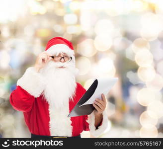 christmas, holidays and people concept - man in costume of santa claus with notepad over lights background