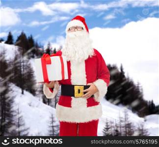 christmas, holidays and people concept - man in costume of santa claus with gift box over snowy mountains background