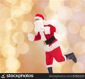 christmas, holidays and people concept - man in costume of santa claus running with bag over beige lights background