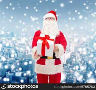 christmas, holidays and people concept - man in costume of santa claus with gift box over snowy city background