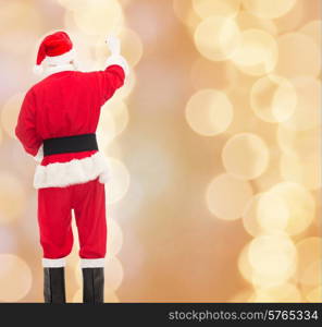 christmas, holidays and people concept - man in costume of santa claus writing something from back over beige lights background