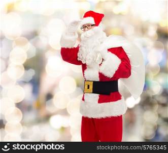 christmas, holidays and people concept - man in costume of santa claus with bag looking far away over lights background